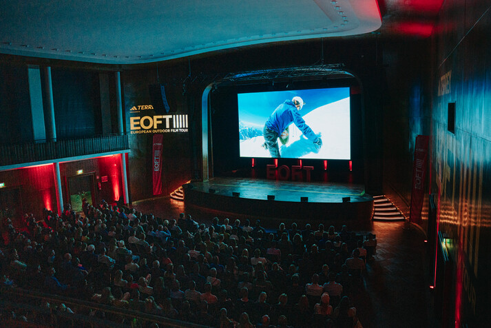 Voller Kinosaal mit Leinwand mit Filmszene von Bergsteiger im Schnee